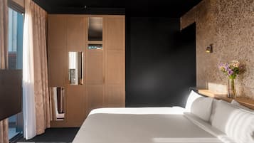 Ein modernes Hotelzimmer mit einem großen Bett, einem Schrank mit Spiegel und einem kleinen Tisch mit Blumen in einer Vase.