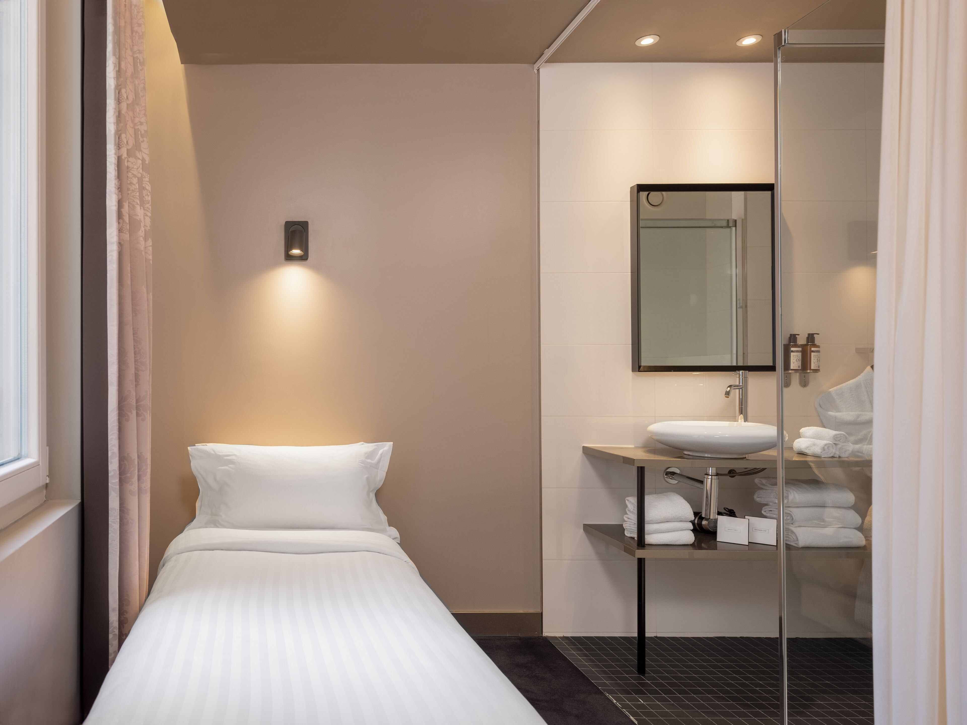 Una habitación de hotel moderna con cama, cabina de ducha de vidrio, lavabo y toallas dobladas con cuidado.