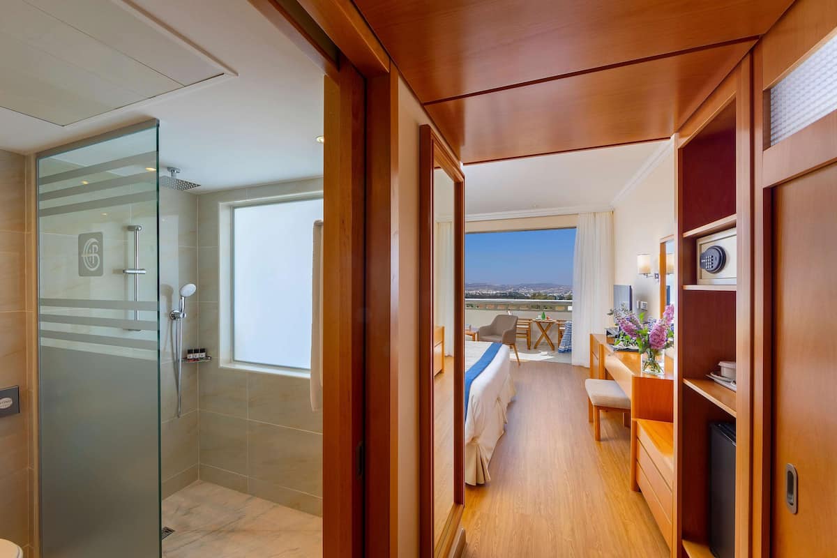 Une chambre d’hôtel dotée d’une douche en verre, d’un balcon avec vue, d’un lit, d’un bureau et d’une télévision.