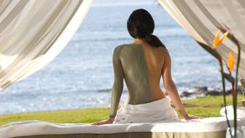A person receiving a back massage on a bed with a view of the sea.