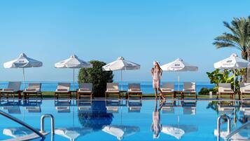 A poolside area with lounge chairs and umbrellas, a clear sky, and a view of the ocean.