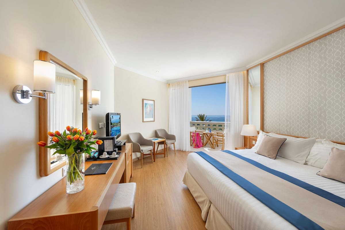 Une chambre d’hôtel équipée d’un lit, d’un bureau, de chaises, d’une télévision et offrant une vue sur l’océan.