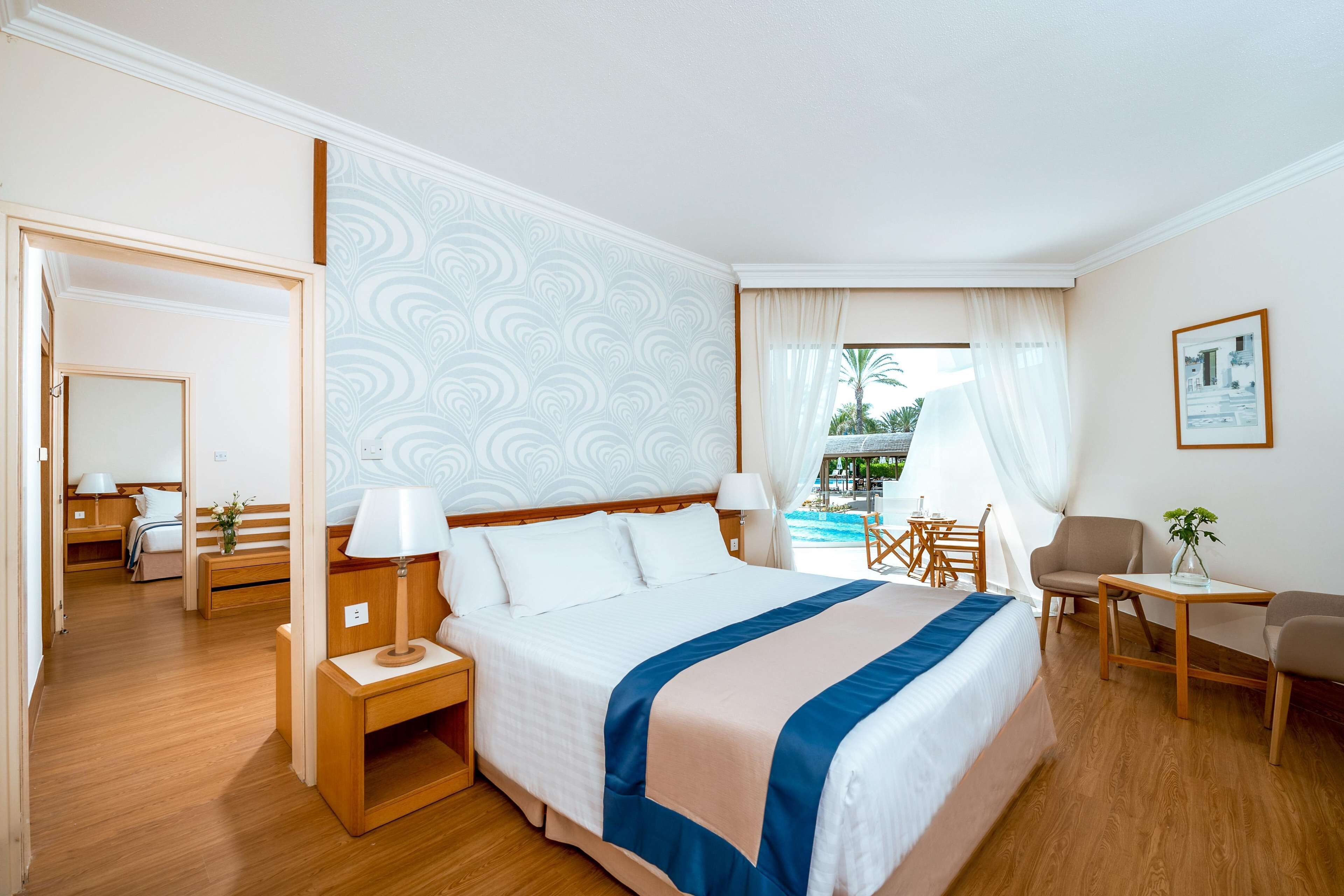 Hotellihuone, jossa on suuri sänky, työpöytä, tuoli, pieni pöytä ja näkymä uima-altaalle.