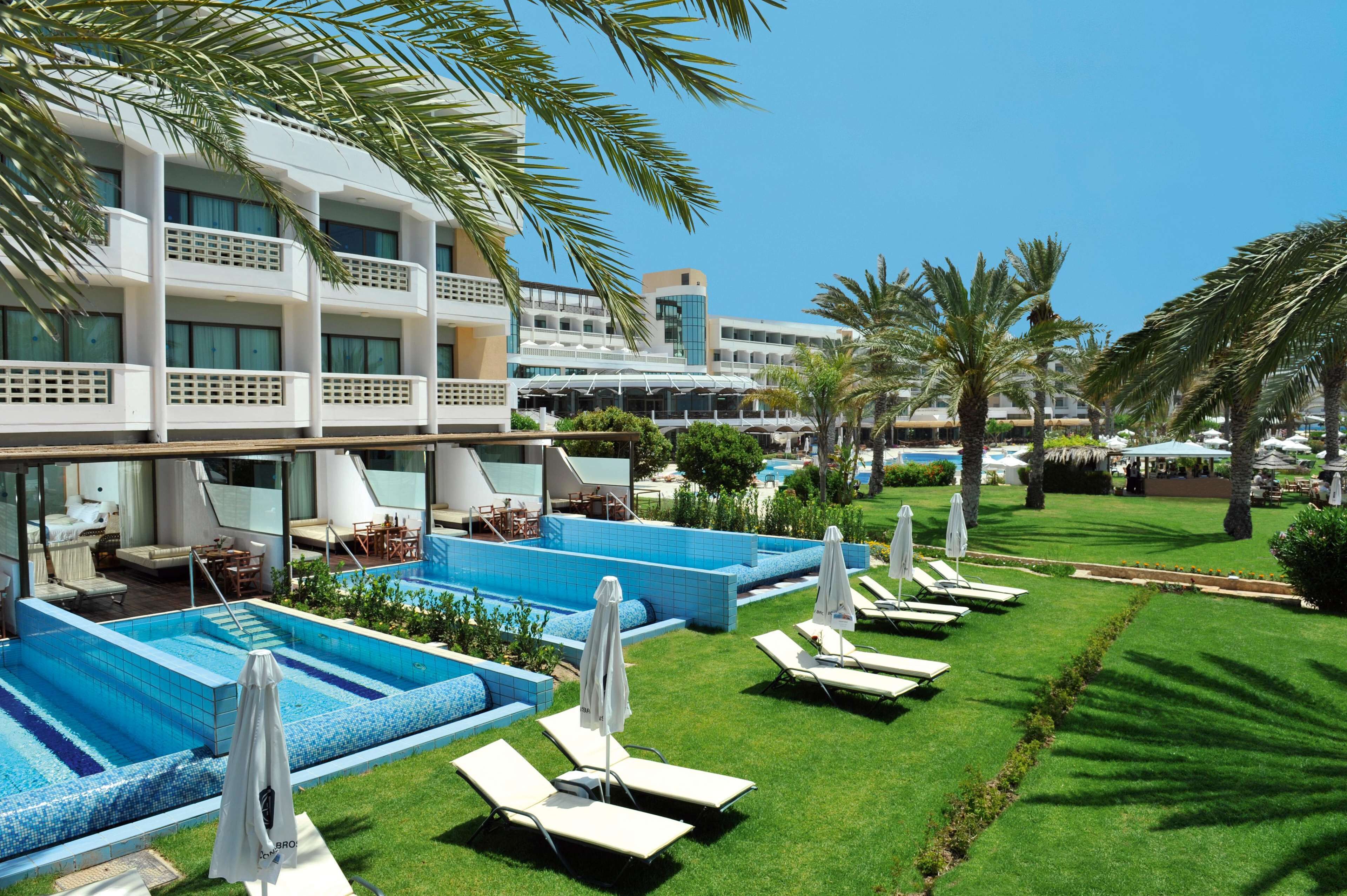 A hotel with multiple swimming pools, sun loungers, and palm trees.