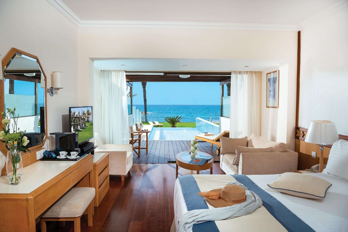 Une chambre d’hôtel avec un lit, un bureau, une chaise, une petite table et une vue sur l’océan.