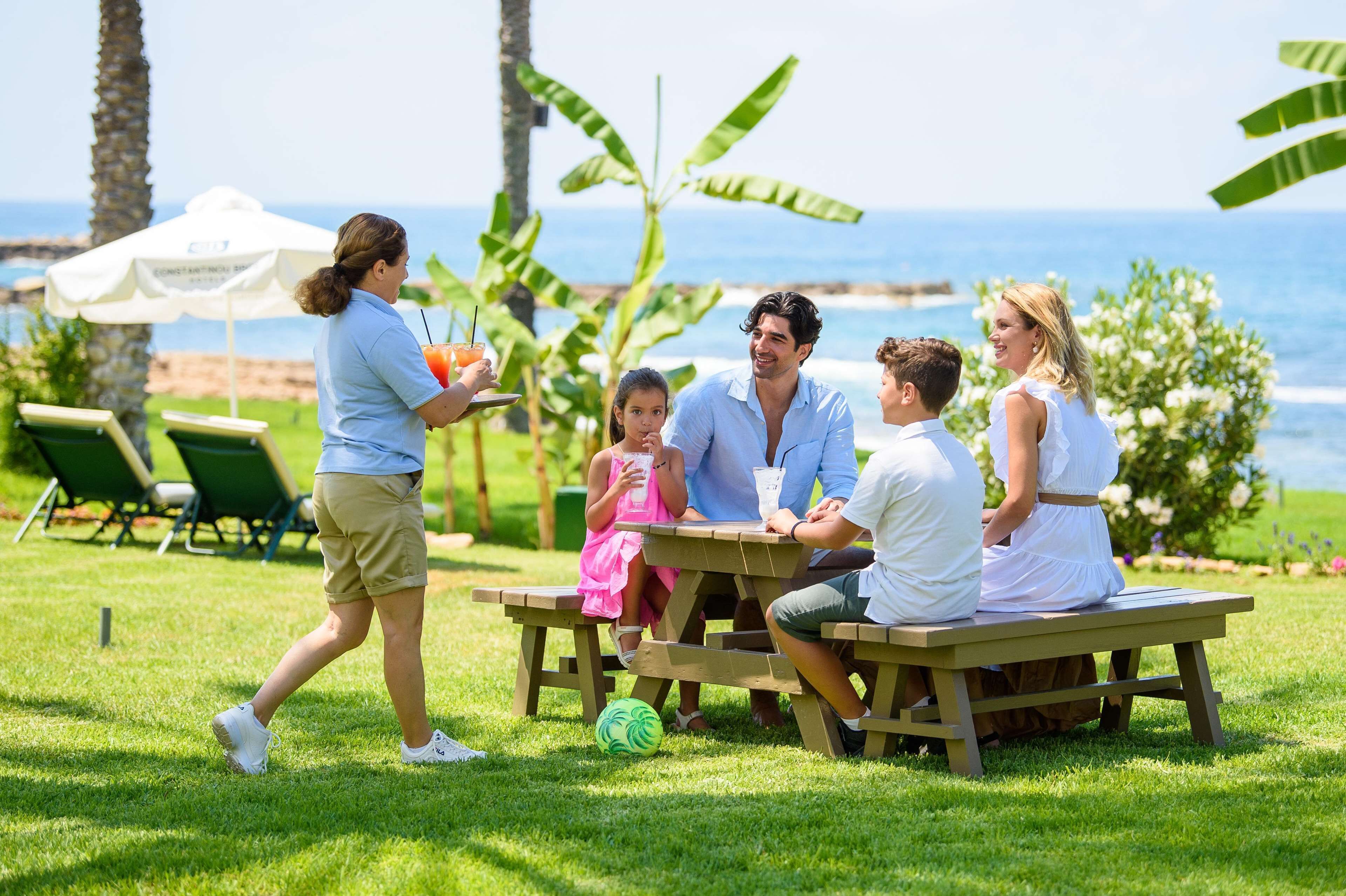 A group of people seated at a picnic table outdoors with a view of the ocean.