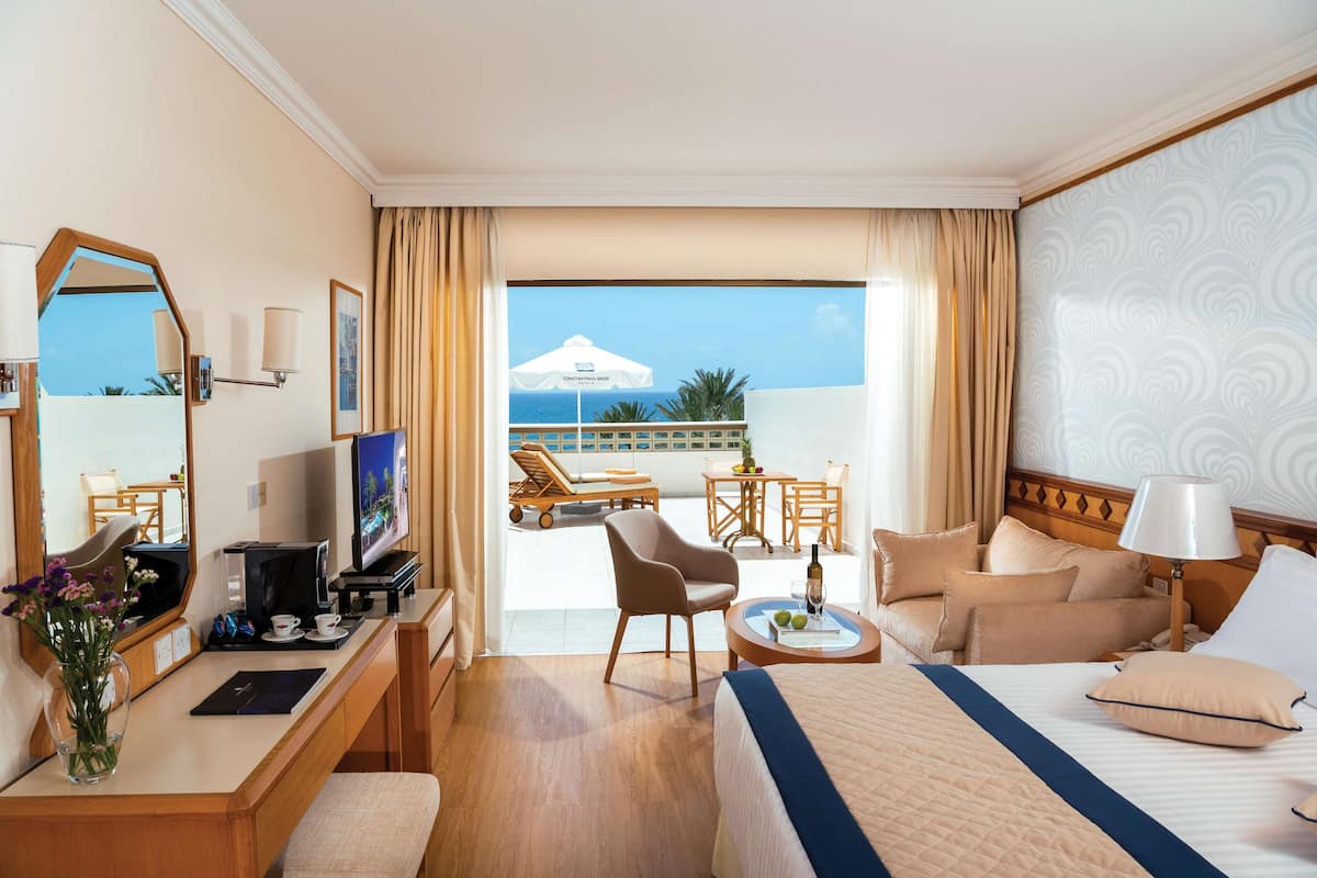 Une chambre d’hôtel équipée d’un lit, d’un bureau, d’une télévision et d’un balcon avec vue sur la mer.