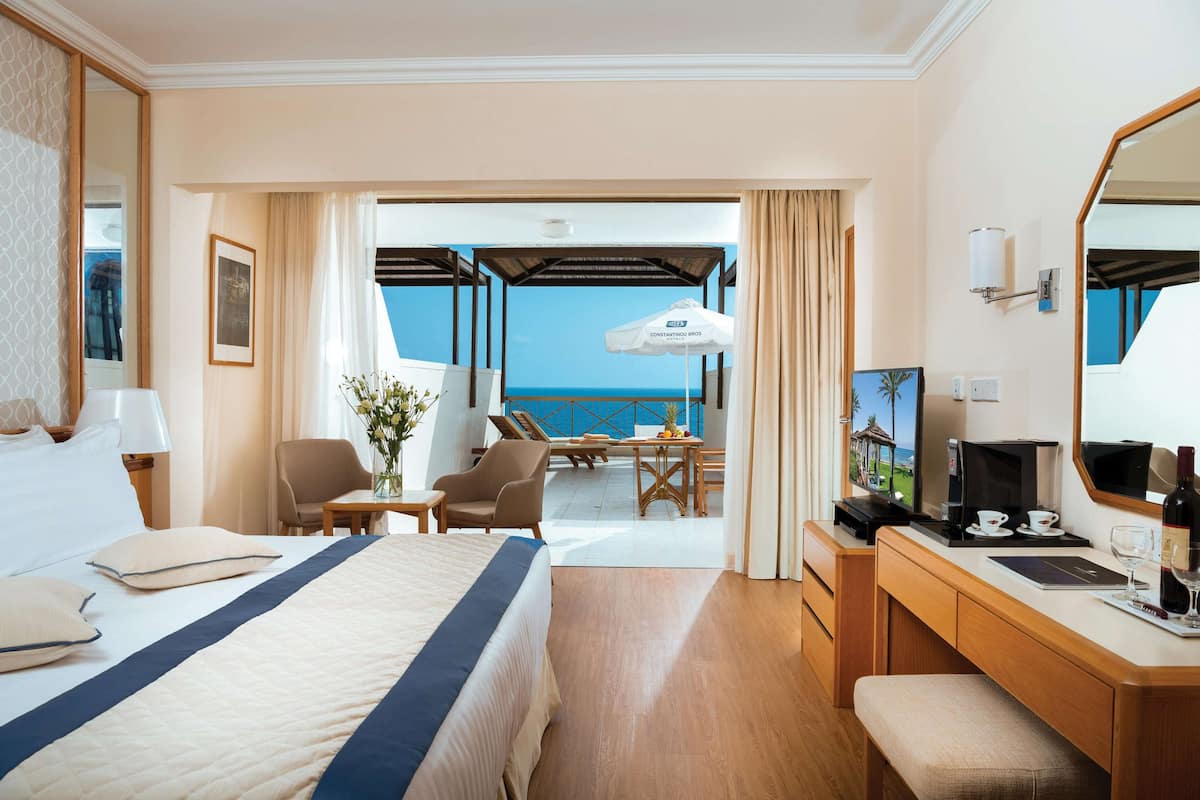 Une chambre d’hôtel avec un lit, un bureau, une chaise, une petite table et une vue sur l’océan.