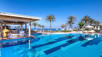 Una piscina con zona de bar, sillas de descanso y palmeras.