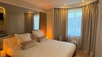 Hotelkamer met een groot bed, nachtkastje, stoel, klein tafeltje met een fles en een spiegel.