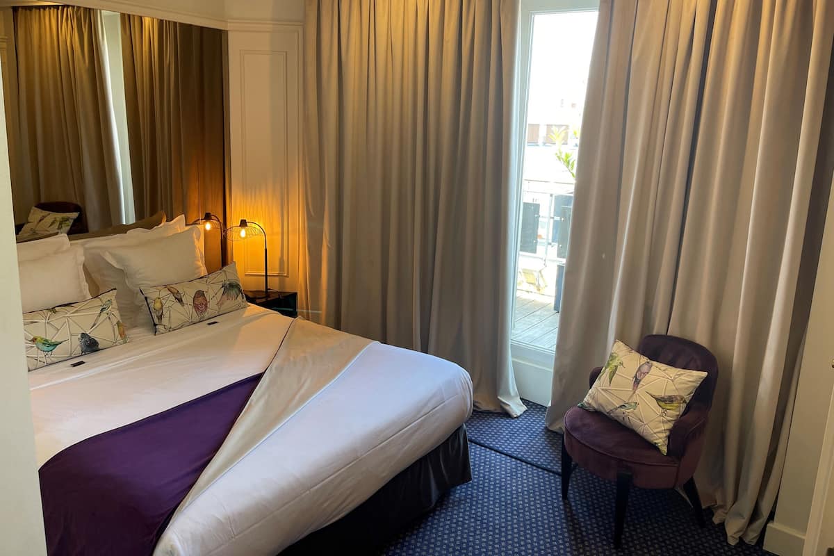 A hotel room with a large bed, two bedside lamps, a chair, and a view of the outside through a glass door.