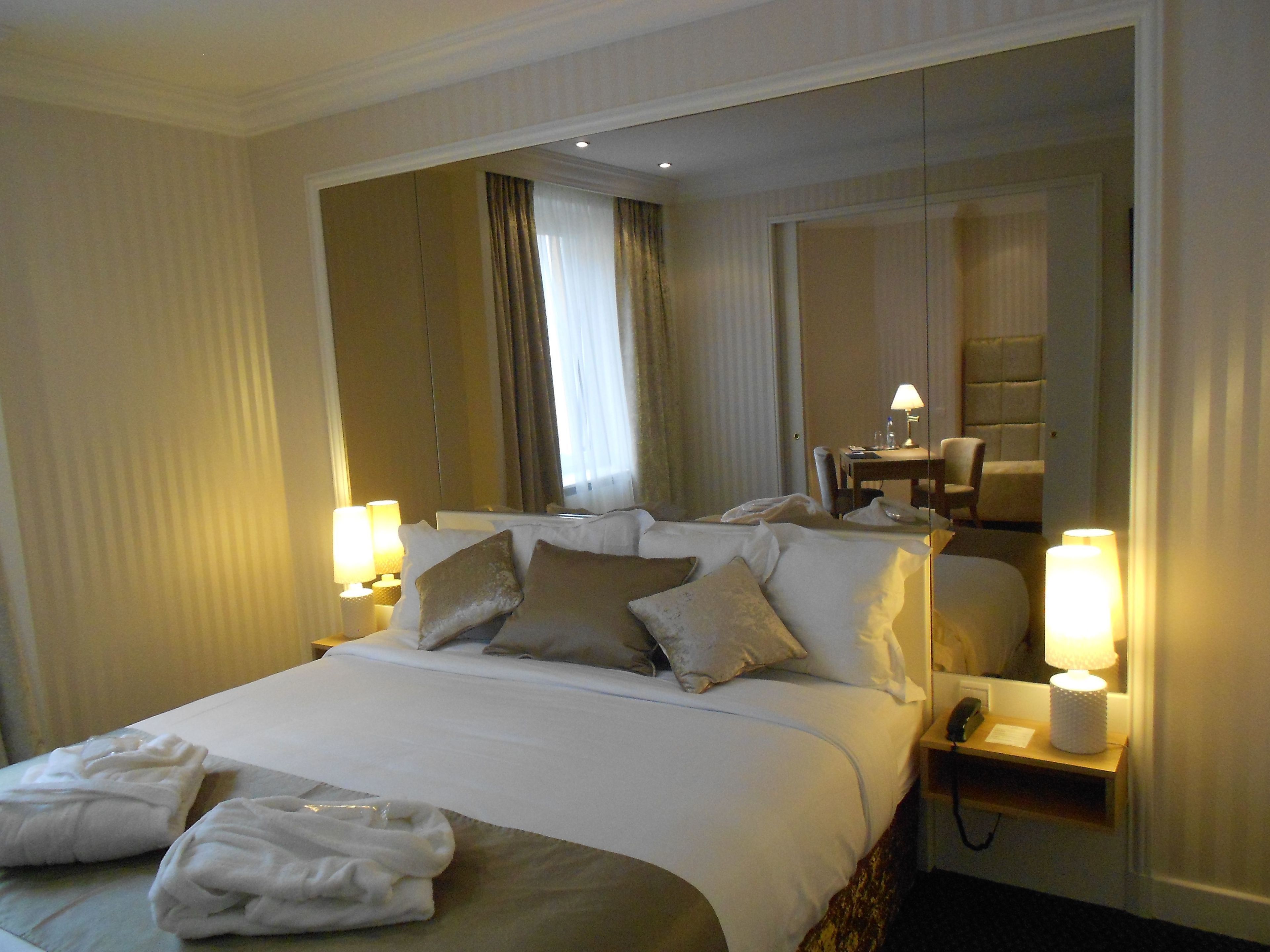 A hotel room with a large bed, two bedside lamps, a bedside telephone, and a mirror above the bed.