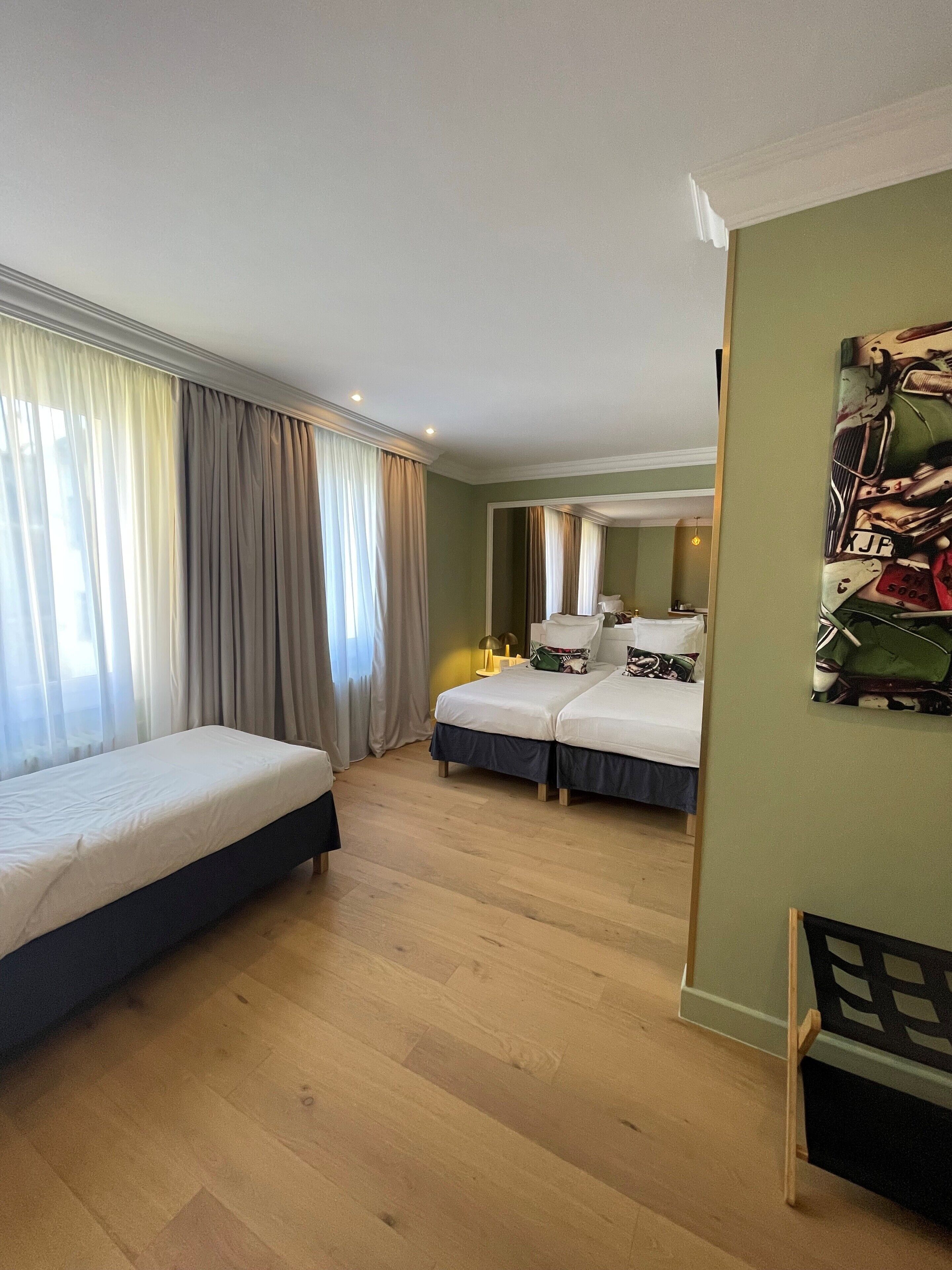 A hotel room with two single beds, a large mirror, and a green wall.