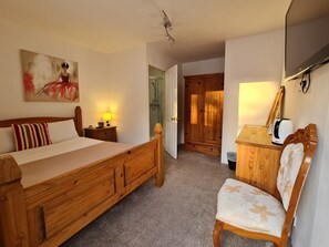 A bedroom with a wooden bed, a nightstand, a chair, a desk, a television, and a painting on the wall. - Pymgate Lodge Hotel (Cheadle)