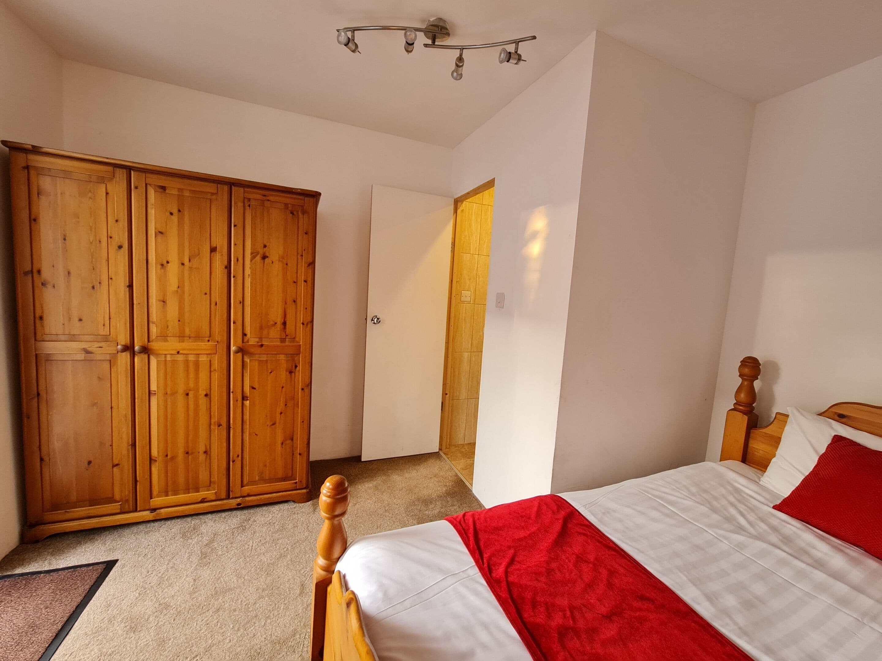 A bedroom with a wooden wardrobe, a bed with white and red bedding, and a ceiling light fixture.