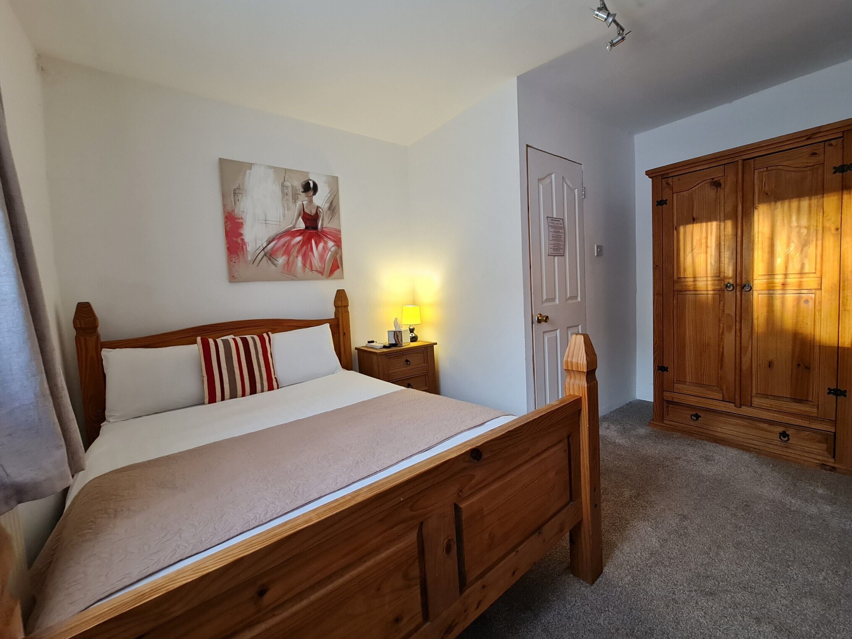 Ein Schlafzimmer mit einem hölzernen Bett, einem Nachttisch mit Lampe, einem Kleiderschrank und einem Gemälde an der Wand.