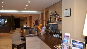A hotel lobby with a reception desk, seating area, and a bar with various bottles and a coffee machine.