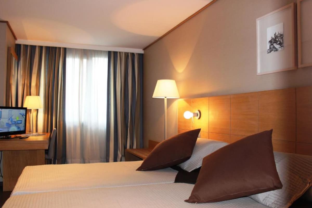 Een hotelkamer met een bed, een bureau met een computer, een lamp en een lijst aan de muur.