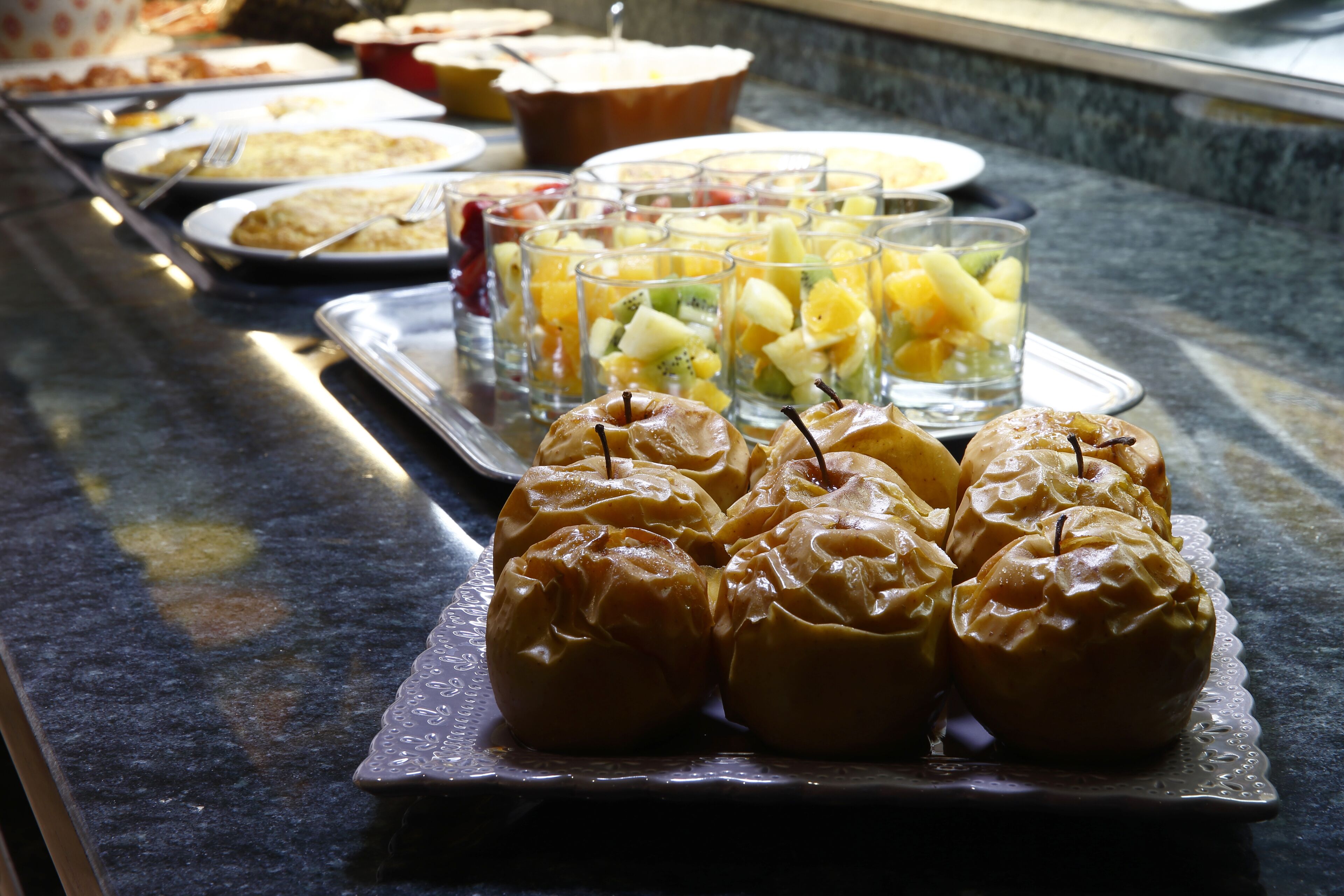 A buffet with various food items including apples and fruit cups.