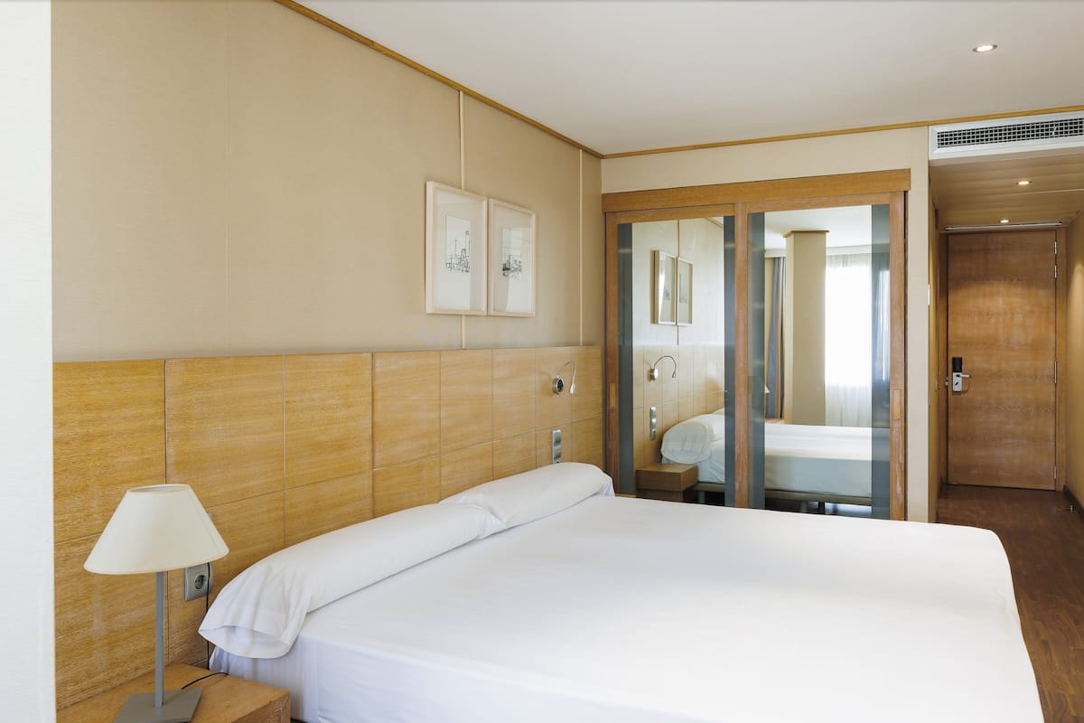 Ein Hotelzimmer mit einem großen Bett, einem Nachttisch mit Lampe, einem Spiegel und einem hölzernen Kopfteil.