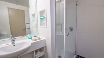 A bathroom with a white sink, a mirror, a glass shower enclosure, and toiletries on the counter.