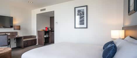 A hotel room with a large bed, a desk, a chair, a TV, and a framed picture on the wall.