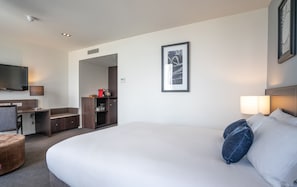 A hotel room with a large bed, a desk, a chair, a TV, and a framed picture on the wall.