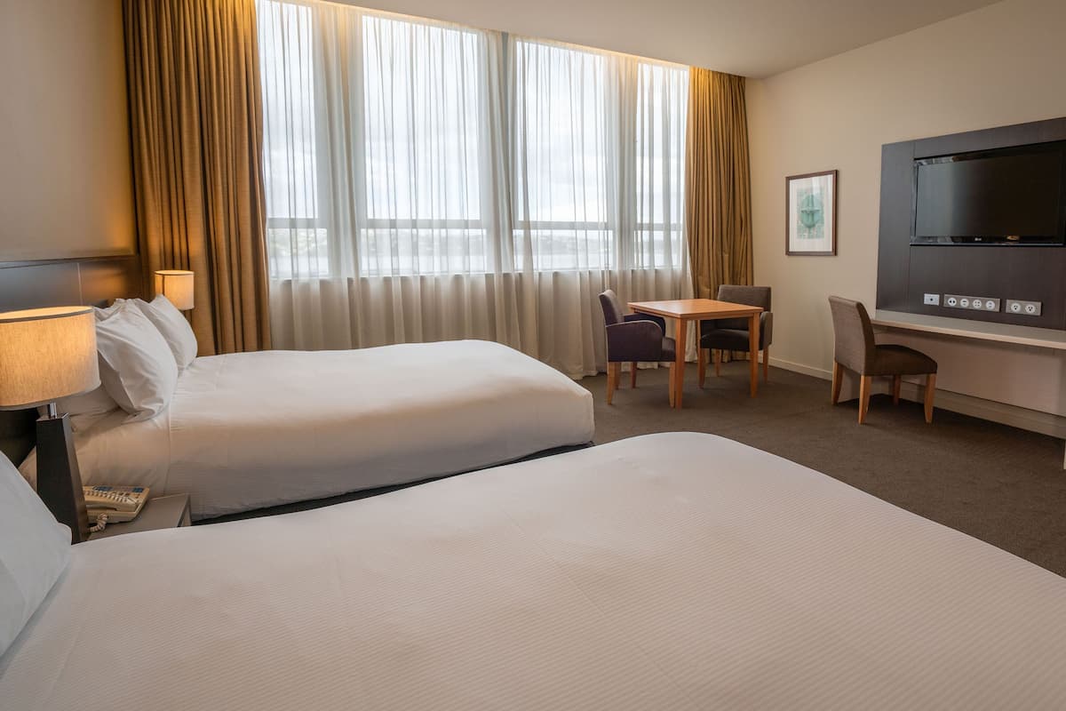 A hotel room with two beds, a desk, a chair, a television, and a window with curtains.