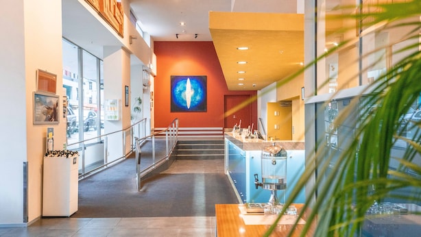 Un interior moderno con una escalera que baja a un nivel inferior, puertas de vidrio y una llamativa obra de arte azul en la pared.