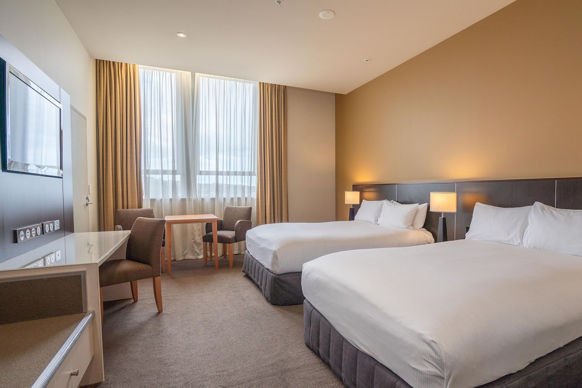 A hotel room with two beds, a desk, a chair, and a small table.