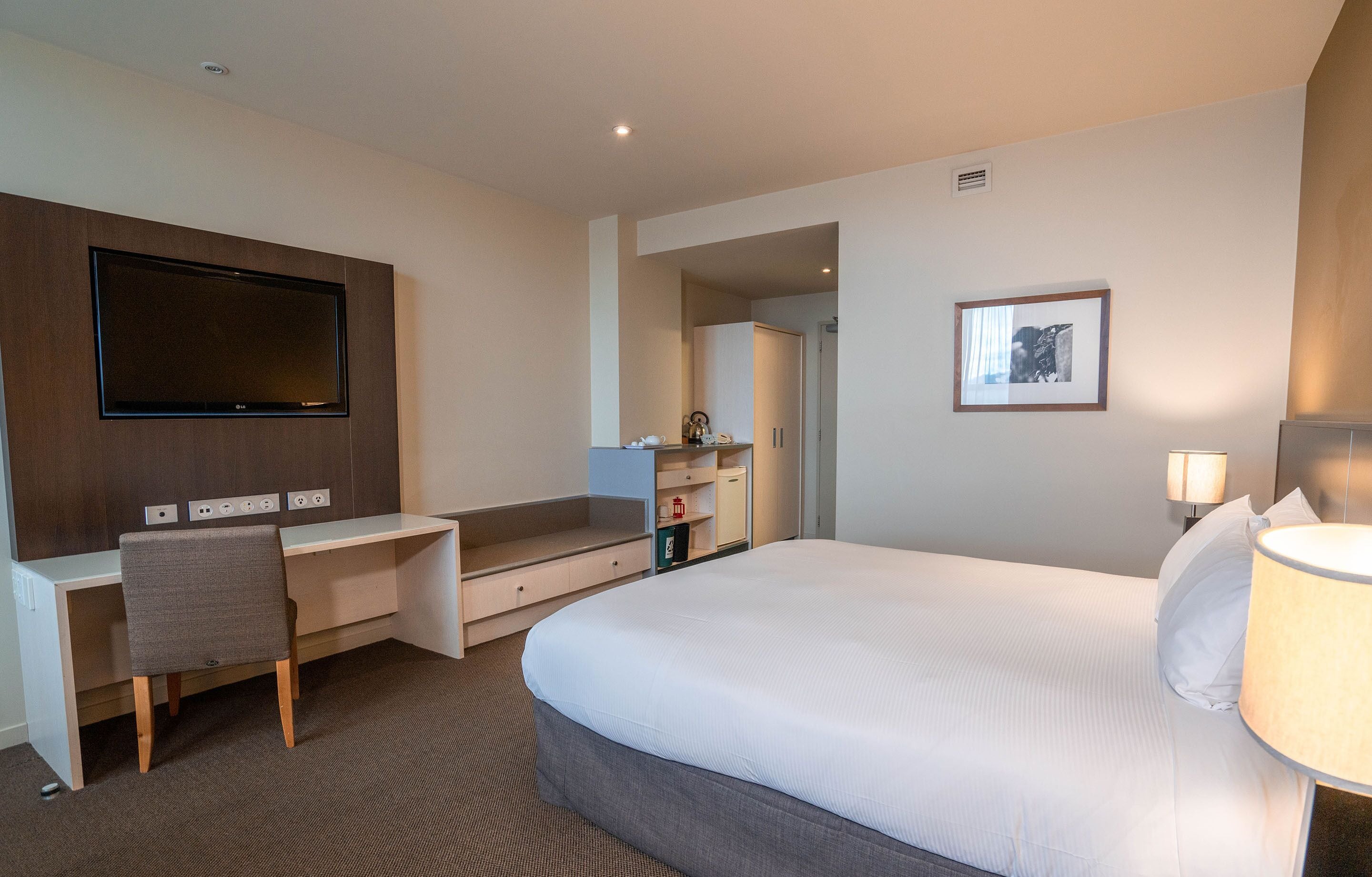 Een hotelkamer met een bed, een bureau, een televisie en een bedlamp.