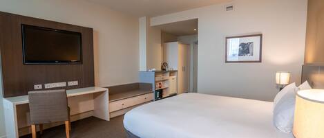 Ein Hotelzimmer mit Bett, Schreibtisch, Fernseher und Nachttischlampe.