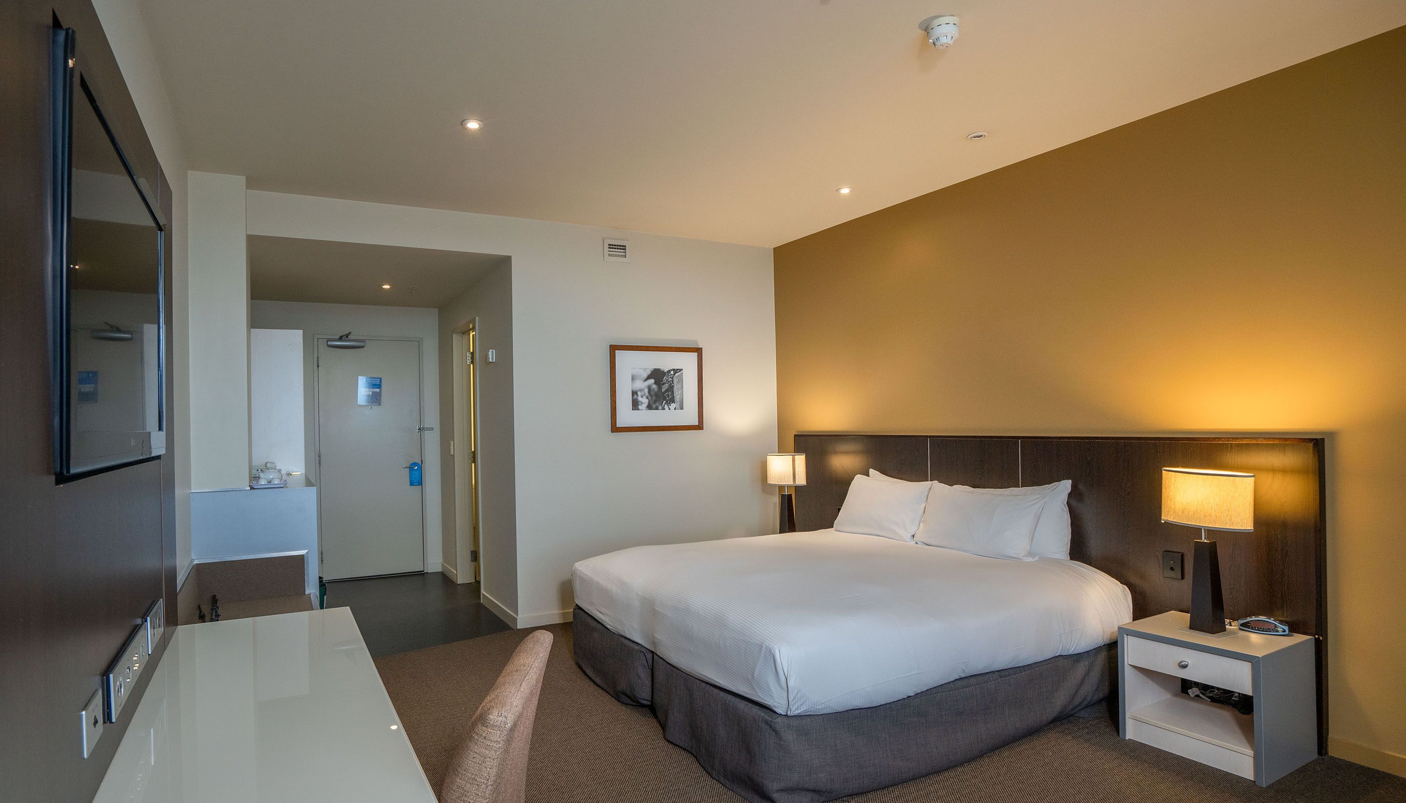 Une chambre d’hôtel comprenant un lit, une table de chevet, une lampe et un bureau avec une chaise.