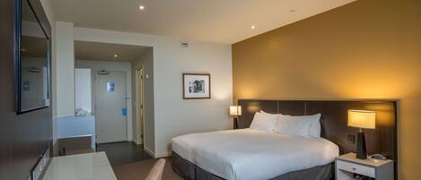 A hotel room with a bed, bedside table, lamp, and a desk with a chair.