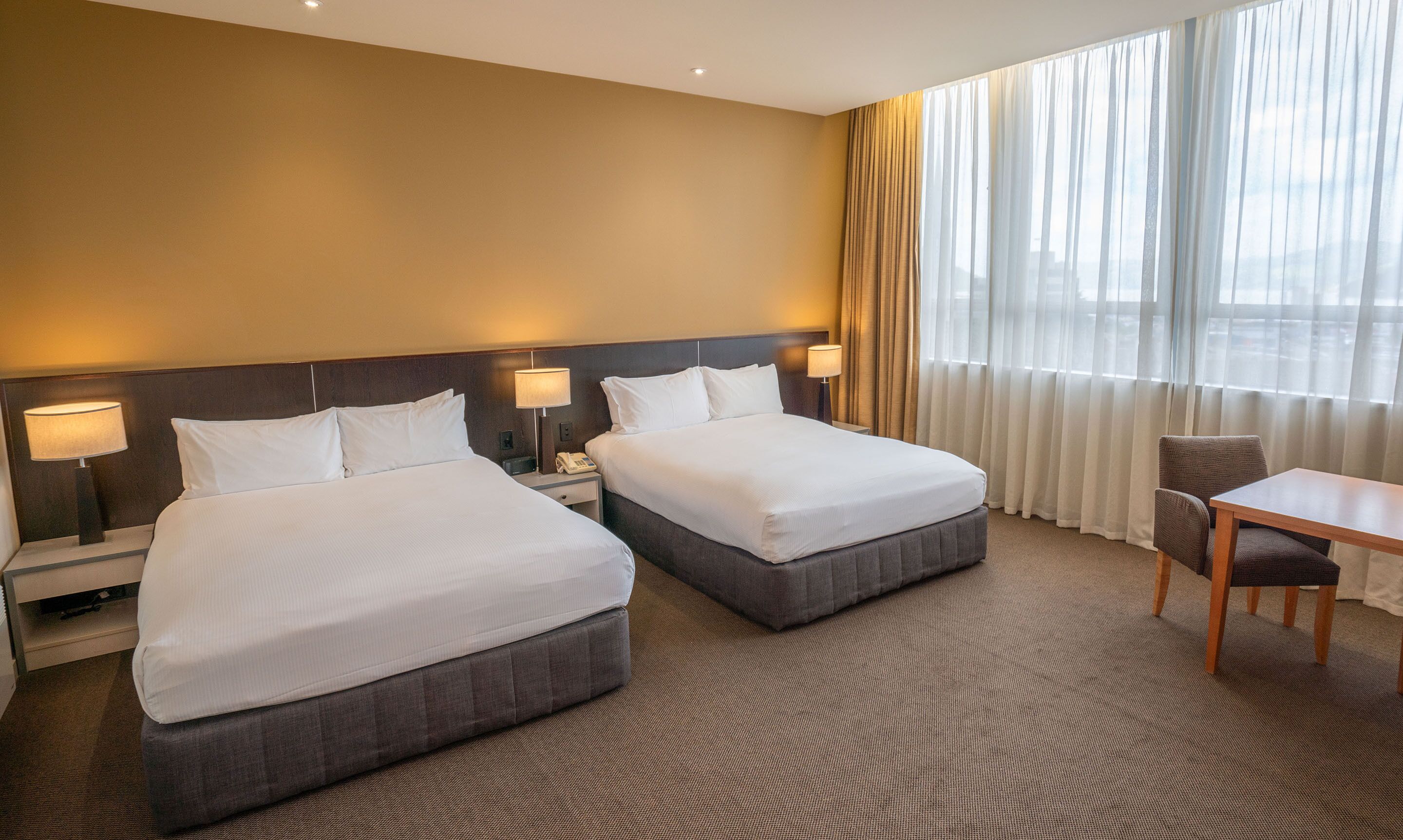 A hotel room with two beds, a desk, and a chair.