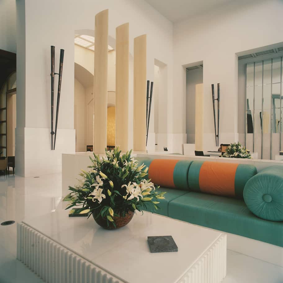 A modern interior with a white sofa, a coffee table with a floral arrangement, and tall, slender columns.