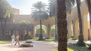 A courtyard with palm trees, a fountain, and a building with arches.