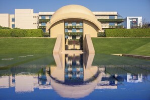 A modern building with a unique dome structure, a reflective pool in front, and a well-maintained lawn.