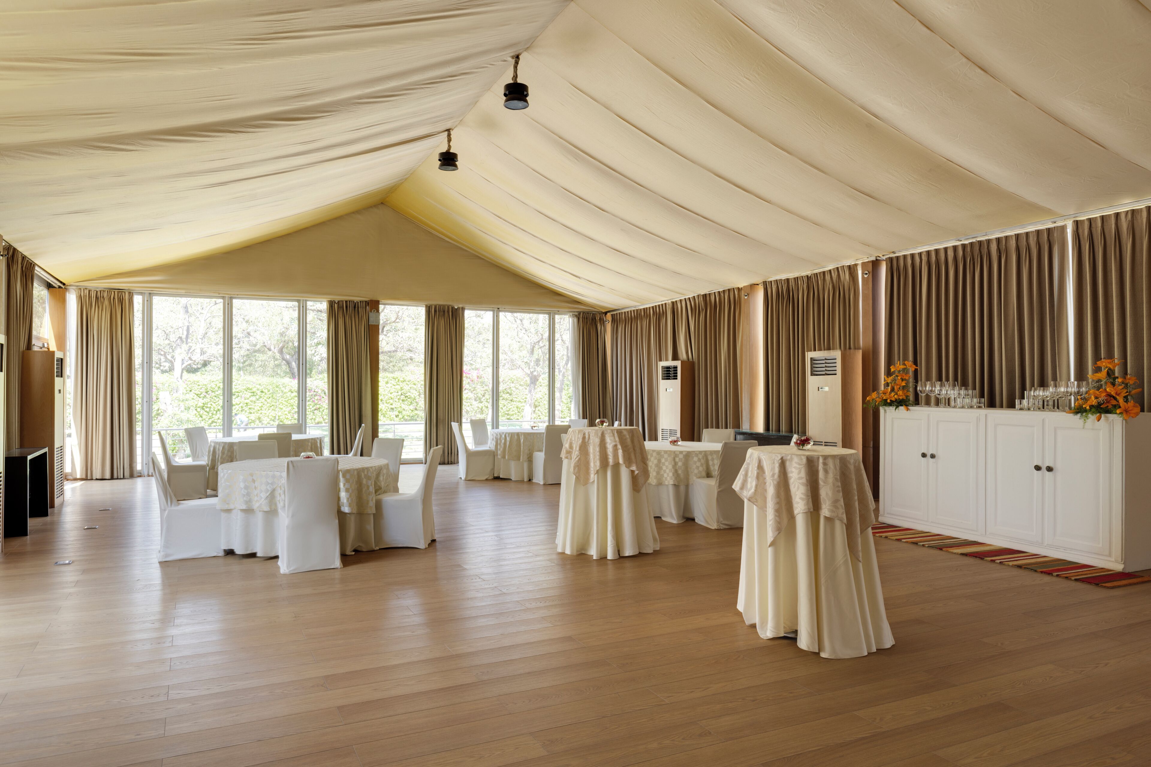 A spacious room with high ceilings, multiple tables set for dining, and a large white cabinet with flowers.