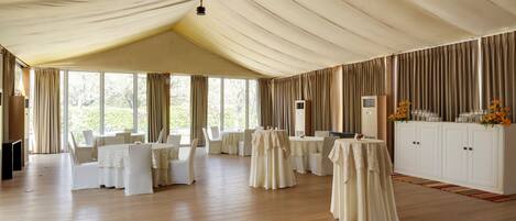 A spacious room with high ceilings, multiple tables set for dining, and a large white cabinet with flowers.