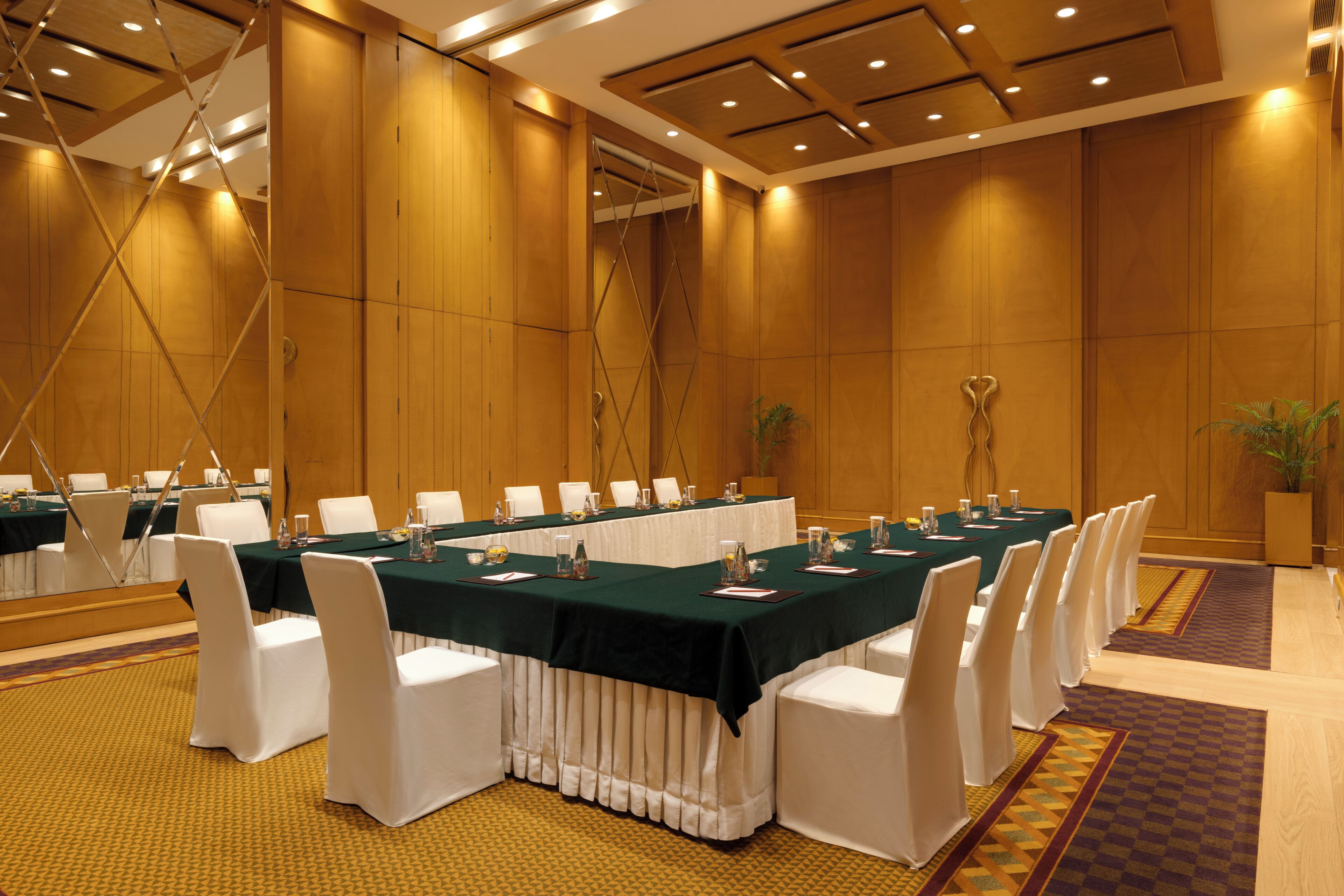 Un salón de conferencias con una larga mesa, sillas blancas y un mantel verde.