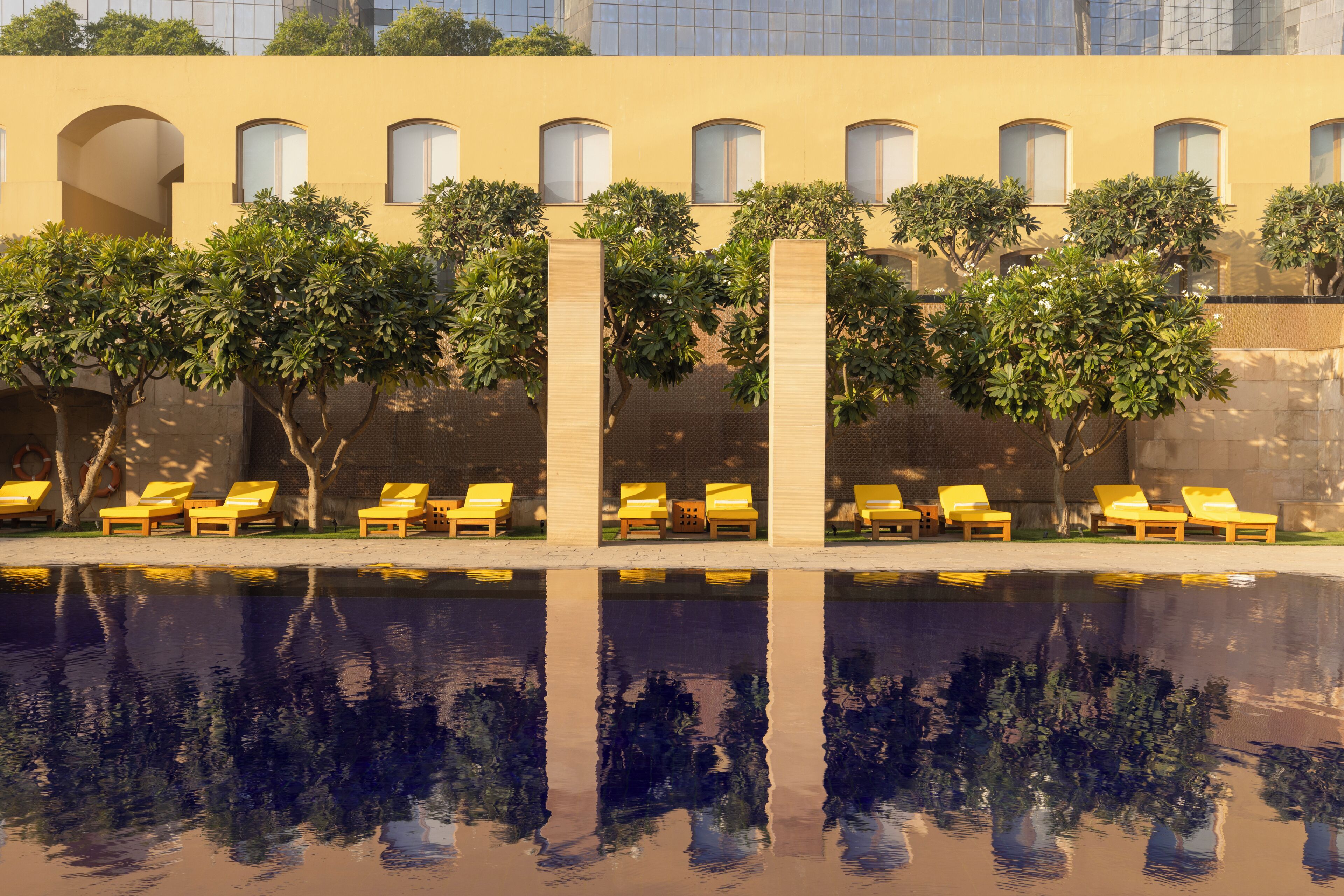 Una piscina amb reflexos, gandules grogues i un edifici amb finestres i arbres.