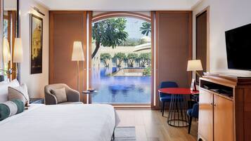 A hotel room with a bed, a desk, a TV, and a view of an outdoor swimming pool.
