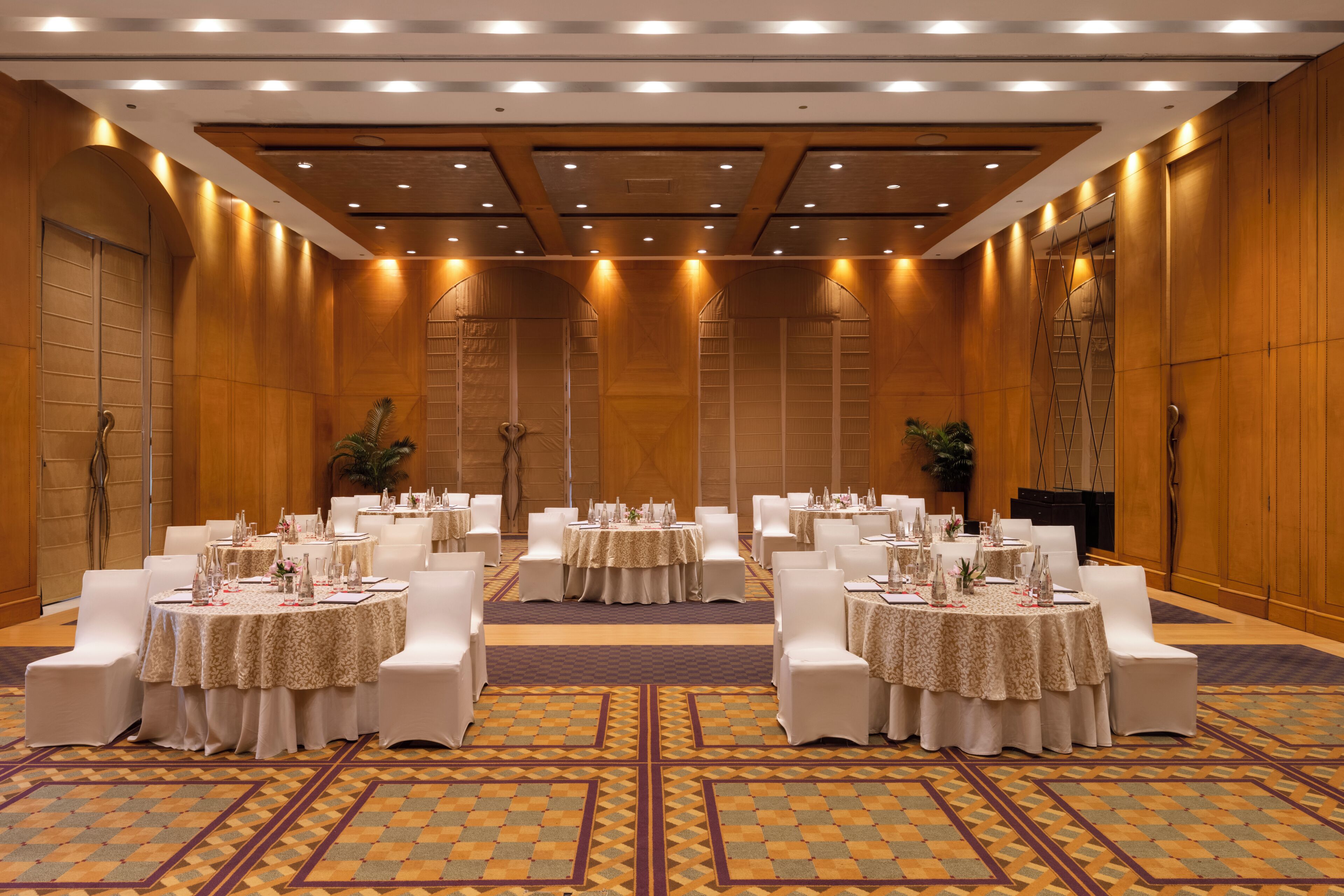 A conference room with multiple round tables, white chairs, and a patterned carpet.