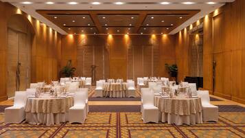 Un salón de conferencias con varias mesas redondas, sillas blancas y una alfombra estampada.