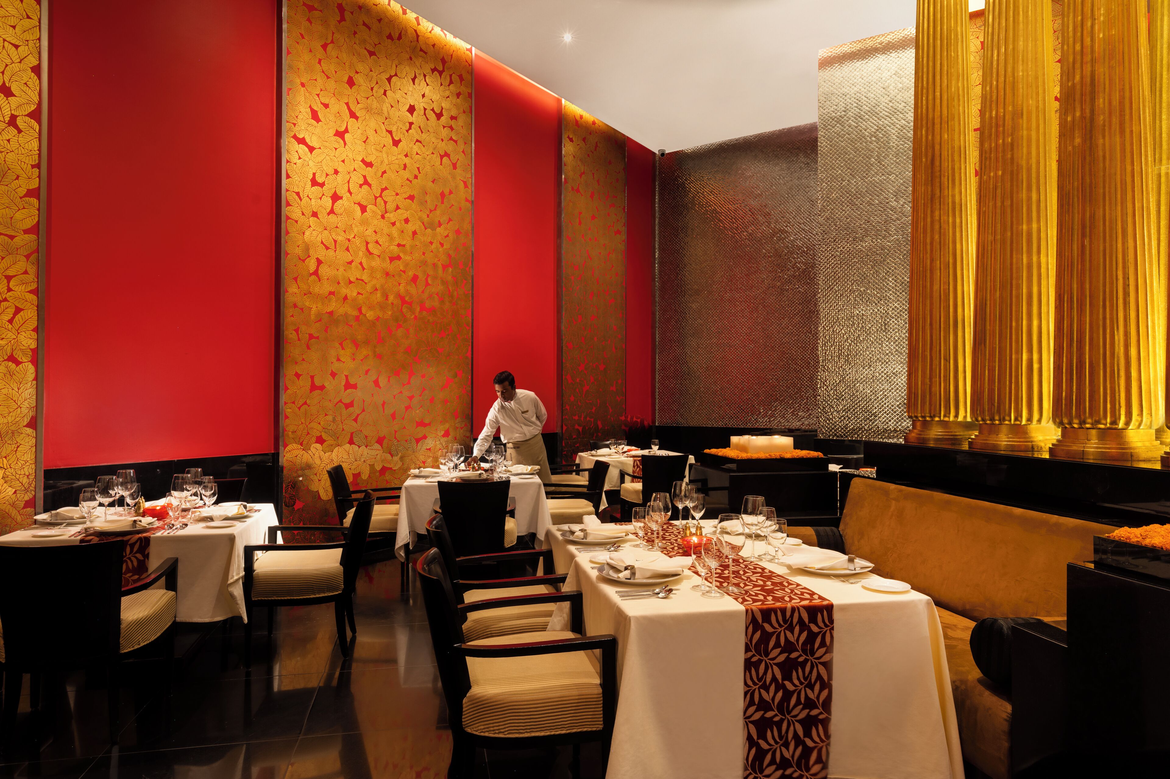 Un restaurante con mesas dispuestas para comer, un camarero atendiendo a los clientes y una pared decorativa con un diseño dorado.