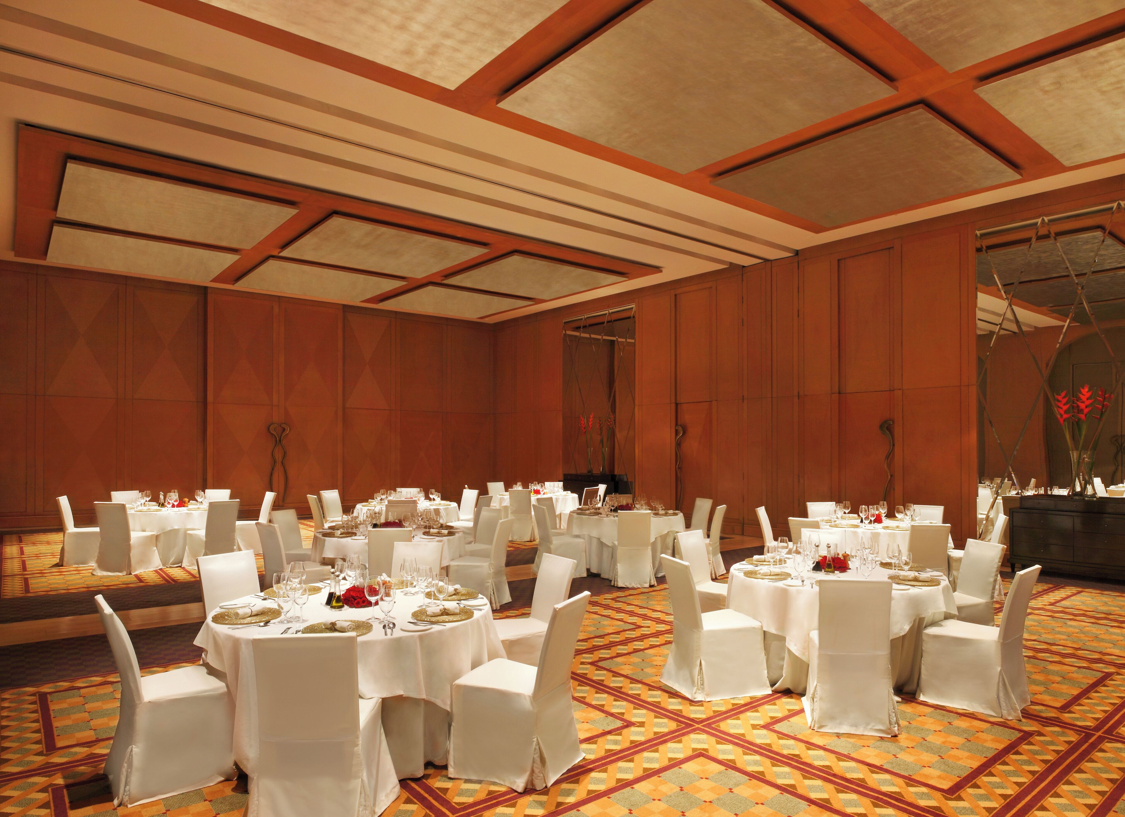 A banquet hall with round tables, white chairs, and a patterned carpet.