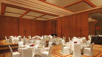 A banquet hall with round tables, white chairs, and a patterned carpet.
