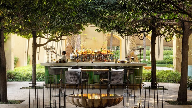 An outdoor bar area with a fountain centerpiece, surrounded by chairs and a variety of bottles.