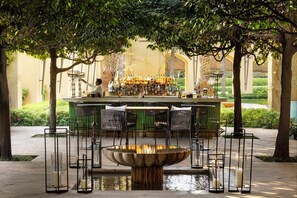 An outdoor bar area with a fountain centerpiece, surrounded by chairs and a variety of bottles.